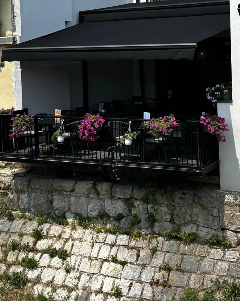 Terasa restorana Terrazza sa tendom i cvećem, iznad kamenog zida keja